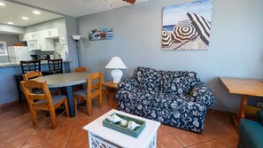 Una sala de estar con un sofá estampado, una mesa de comedor con sillas, una zona de cocina y un cuadro en la pared.
