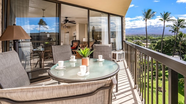 A balcony with a glass table, chairs, and a potted plant.
