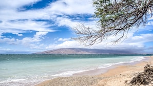 A beach with clear turquoise water, a sandy shore, and a distant mountain.