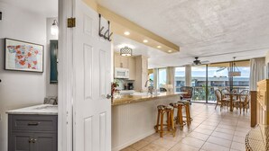 A modern kitchen with a white countertop, grey cabinets, and a bar area with stools.