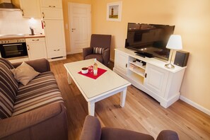 A living room with a sofa, a coffee table, a TV, and a kitchen area with cabinets and a stove.