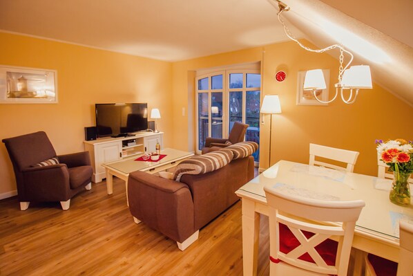 A cozy living room with a sofa, armchairs, a TV, and a dining table with chairs.