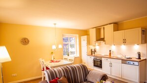 A compact living space with a dining area, sofa, kitchen, and a clock on the wall. - Int Corner 6 (Krummhörn)