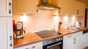 A modern kitchen with white cabinets, a wooden countertop, a built-in oven, and a stovetop. - Int Corner 6 (Krummhörn)