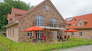 A two-story brick house with a balcony, red outdoor furniture, and a fenced garden area. - Int Corner 7 (Krummhörn)