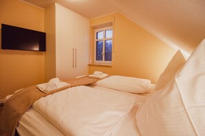 A hotel room with two beds, a flat-screen TV mounted on the wall, a window with a view, and a wooden headboard.