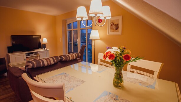 Una sala de estar acogedora con un sofá, una mesa de comedor con un mapa, un televisor y un florero con flores.