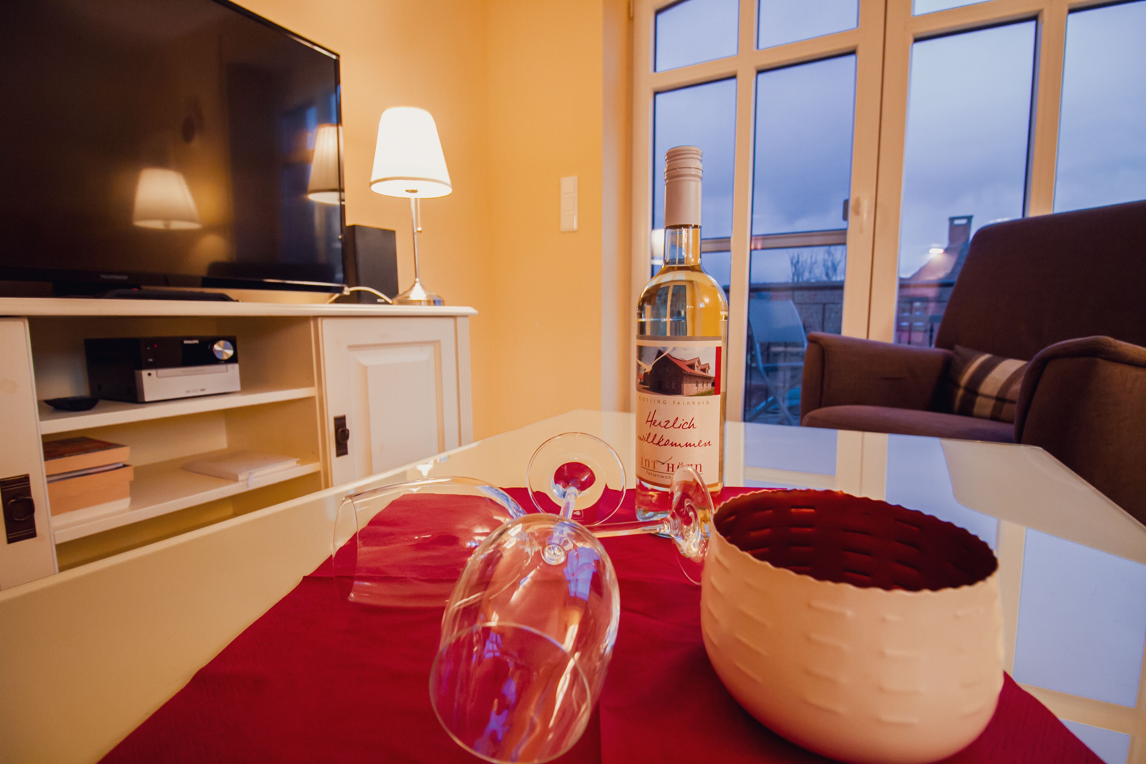 A living room with a television, a bottle of wine, a glass, and a red tablecloth.