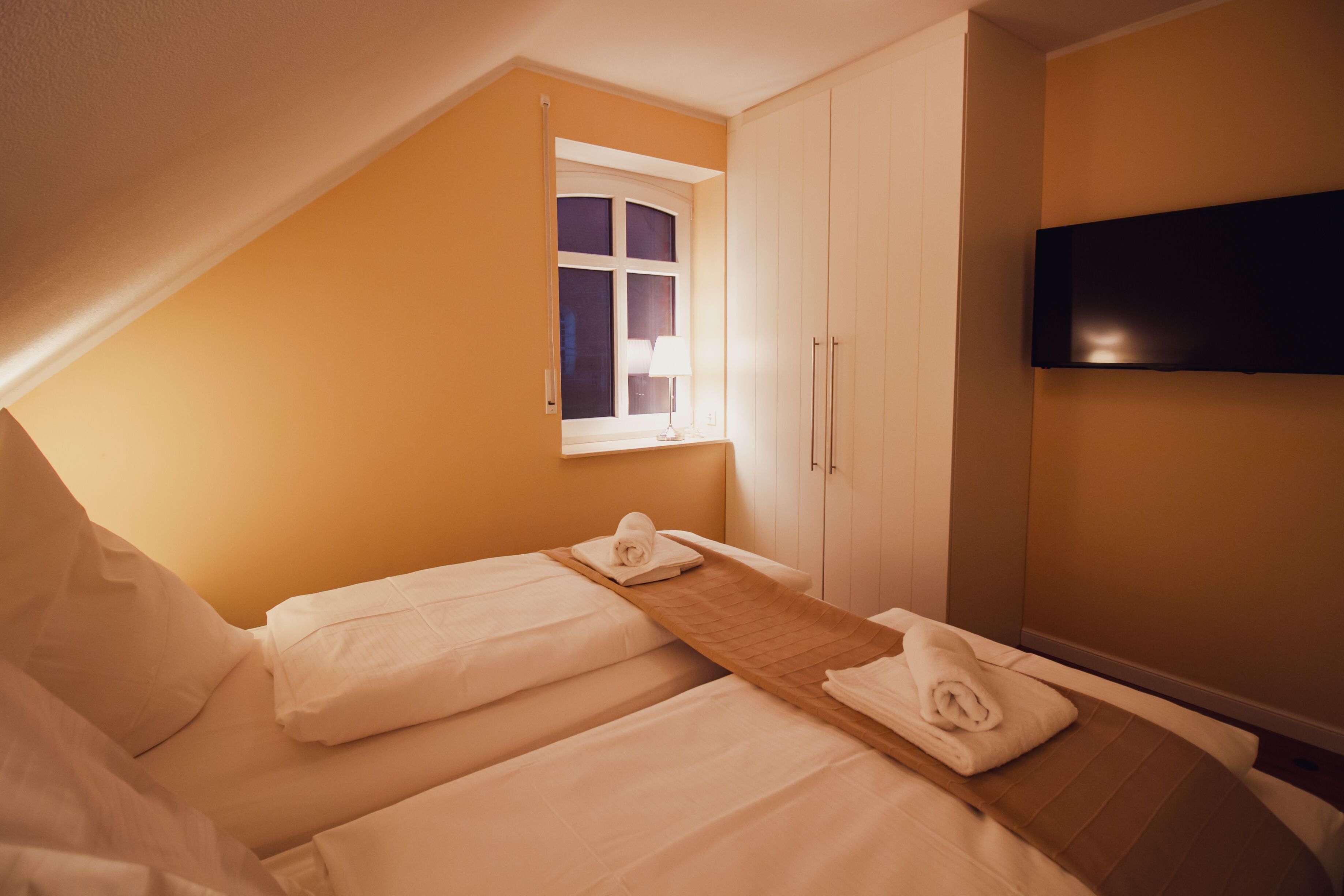 A hotel room with two beds, a window, a TV, and a wardrobe.