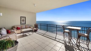 A balcony with a sofa, chairs, and a table, overlooking a clear blue sea. - Phoenix West 2101 | 4BR/4BA Gulf-Front Condo | Oversized Balcony + Lazy River (Orange Beach)
