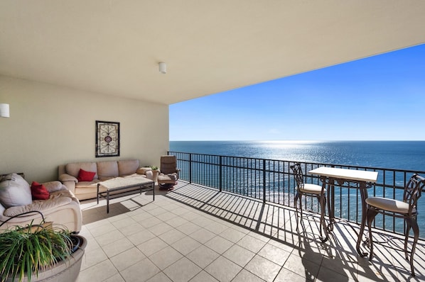 A balcony with a sofa, chairs, and a table, overlooking a clear blue sea.