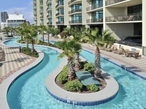 A swimming pool with a curved design, surrounded by palm trees and lounge chairs.
