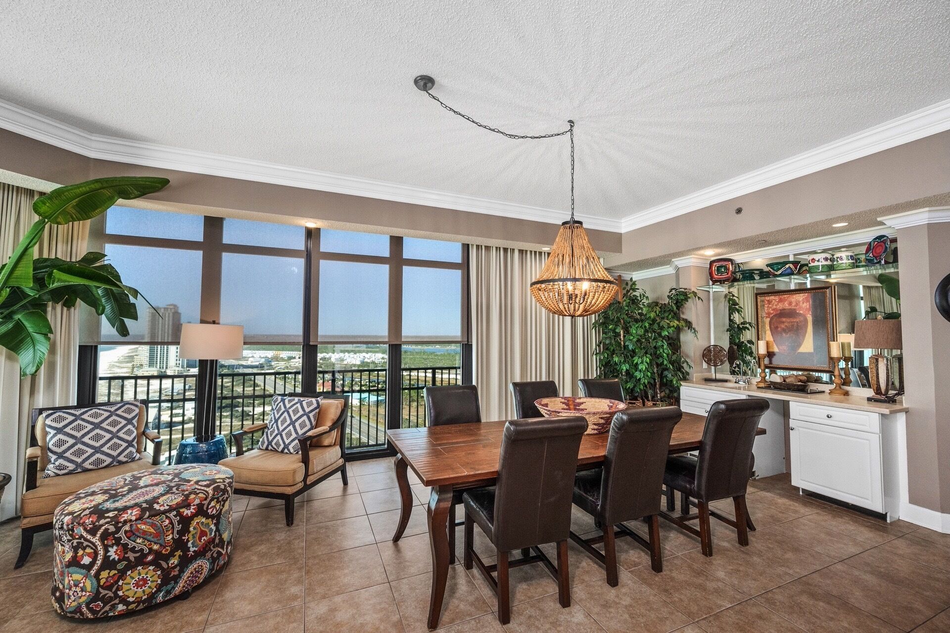 A spacious dining area with a large table and chairs, a hanging light fixture, and a view of the city through large windows.