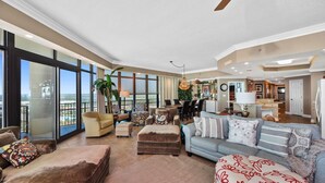 A spacious living room with a large window, a ceiling fan, and a view of the city. - Phoenix West 2101 | 4BR/4BA Gulf-Front Condo | Oversized Balcony + Lazy River (Orange Beach)