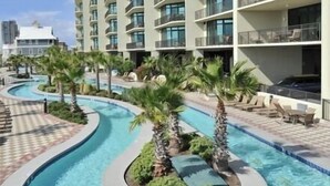 A swimming pool with a curved design, surrounded by palm trees and lounge chairs. - Phoenix West 2101 | 4BR/4BA Gulf-Front Condo | Oversized Balcony + Lazy River (Orange Beach)