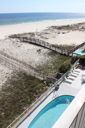 A pool area with a view of the beach and a wooden deck.