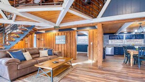 A spacious living area with a wooden staircase, a kitchen with dark cabinetry, and a dining area with wooden furniture. - Balsam Retreat -Charming, Stylish, Great Location! (Maggie Valley)