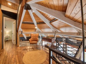 Cozy attic space with a loft-style living area, featuring a wooden floor, leather armchair, and staircase.