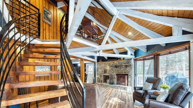 A spacious living area with a wooden staircase, a stone fireplace, and leather sofas. - Balsam Retreat -Charming, Stylish, Great Location! (Maggie Valley)