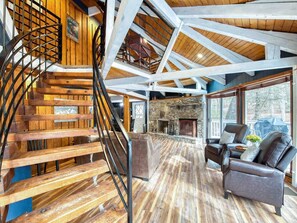 A spacious living area with a wooden staircase, a stone fireplace, and leather sofas. - Balsam Retreat -Charming, Stylish, Great Location! (Maggie Valley)