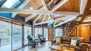 A spacious living room with a wooden floor, large windows, a staircase, and leather furniture. - Balsam Retreat -Charming, Stylish, Great Location! (Maggie Valley)