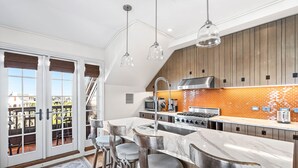 Une cuisine moderne dotée d’un grand îlot central, de tabourets de bar et offrant une vue sur l’extérieur grâce à de grandes portes-fenêtres coulissantes.