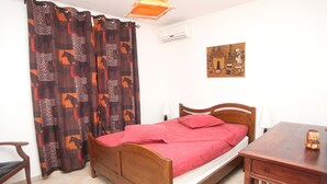 A bedroom with a wooden bed, a red bedspread, a wooden nightstand, a chair, and a wall-mounted air conditioner. - Prestige villa with pool and jacuzzi (LE MOULE)