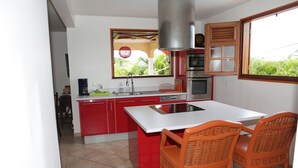 A kitchen with red cabinets, a white island, wicker chairs, and a window with a view of greenery. - Prestige villa with pool and jacuzzi (LE MOULE)