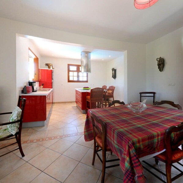 A spacious room with a kitchen area, a dining table with chairs, and a large window providing natural light.