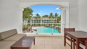 A balcony with a view of a pool, a wooden table, and a sofa.
