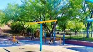 Ein Spielplatz mit Schaukeln und Klettergerüsten, umgeben von Bäumen und einem eingezäunten Bereich.