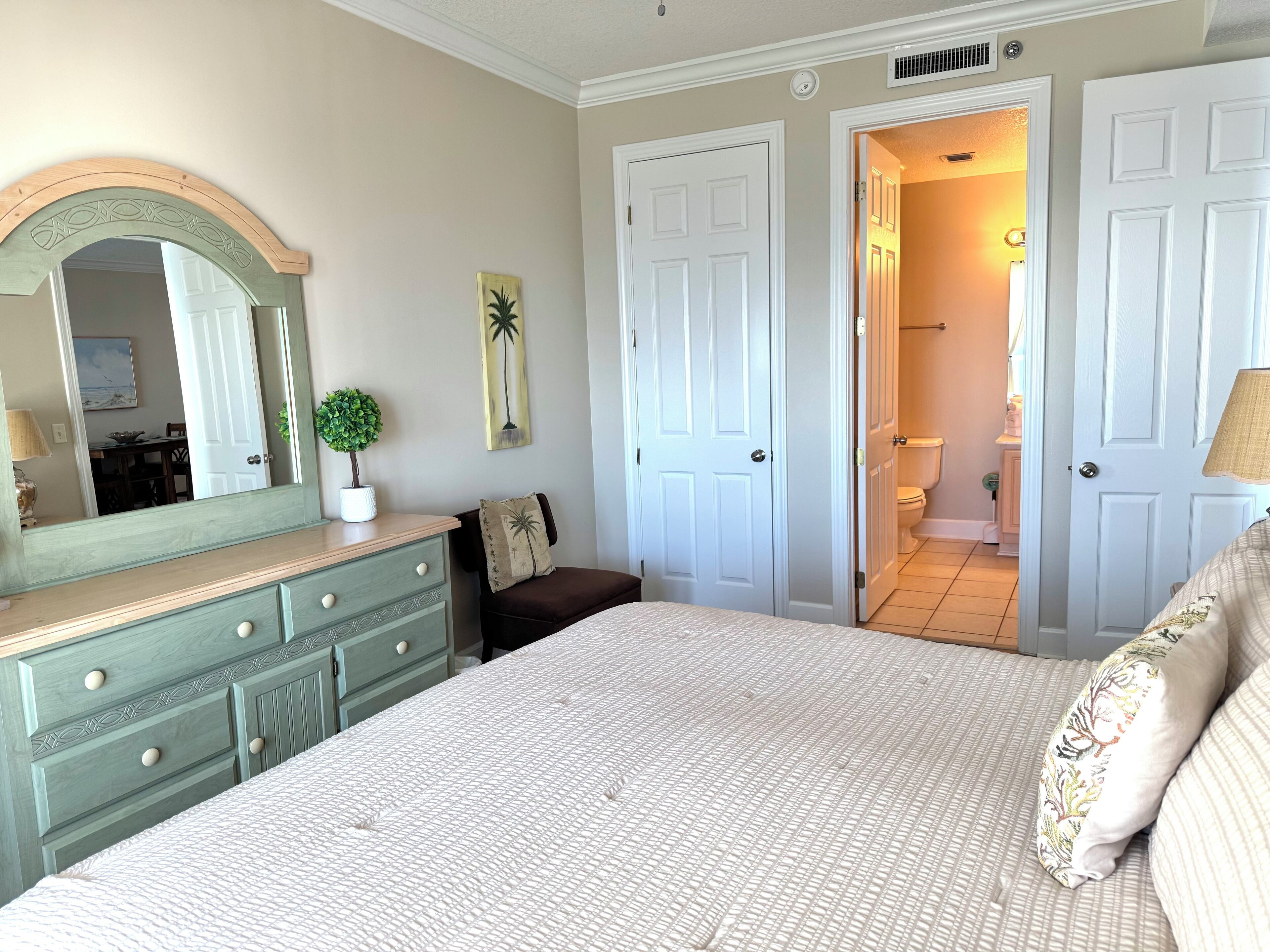 Un dormitorio con cama, cómoda y espejo. Hay dos puertas que dan a otras habitaciones.