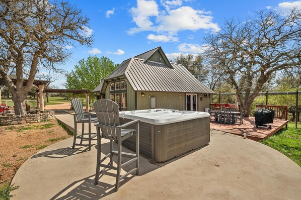A hot tub with a pergola and chairs, a barbecue grill, and a covered patio area.