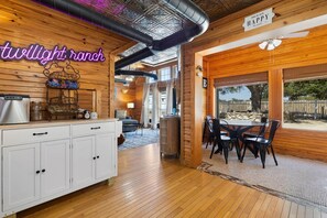Un intérieur en bois agrémenté d’un panneau néon indiquant « Twilight Ranch », un espace repas avec des tables et des chaises, et une vue sur l’extérieur grâce à de grandes fenêtres.