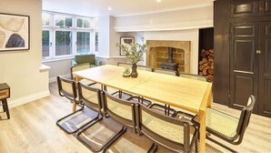 Un comedor con mesa y sillas de madera, chimenea y un ventanal con persianas.