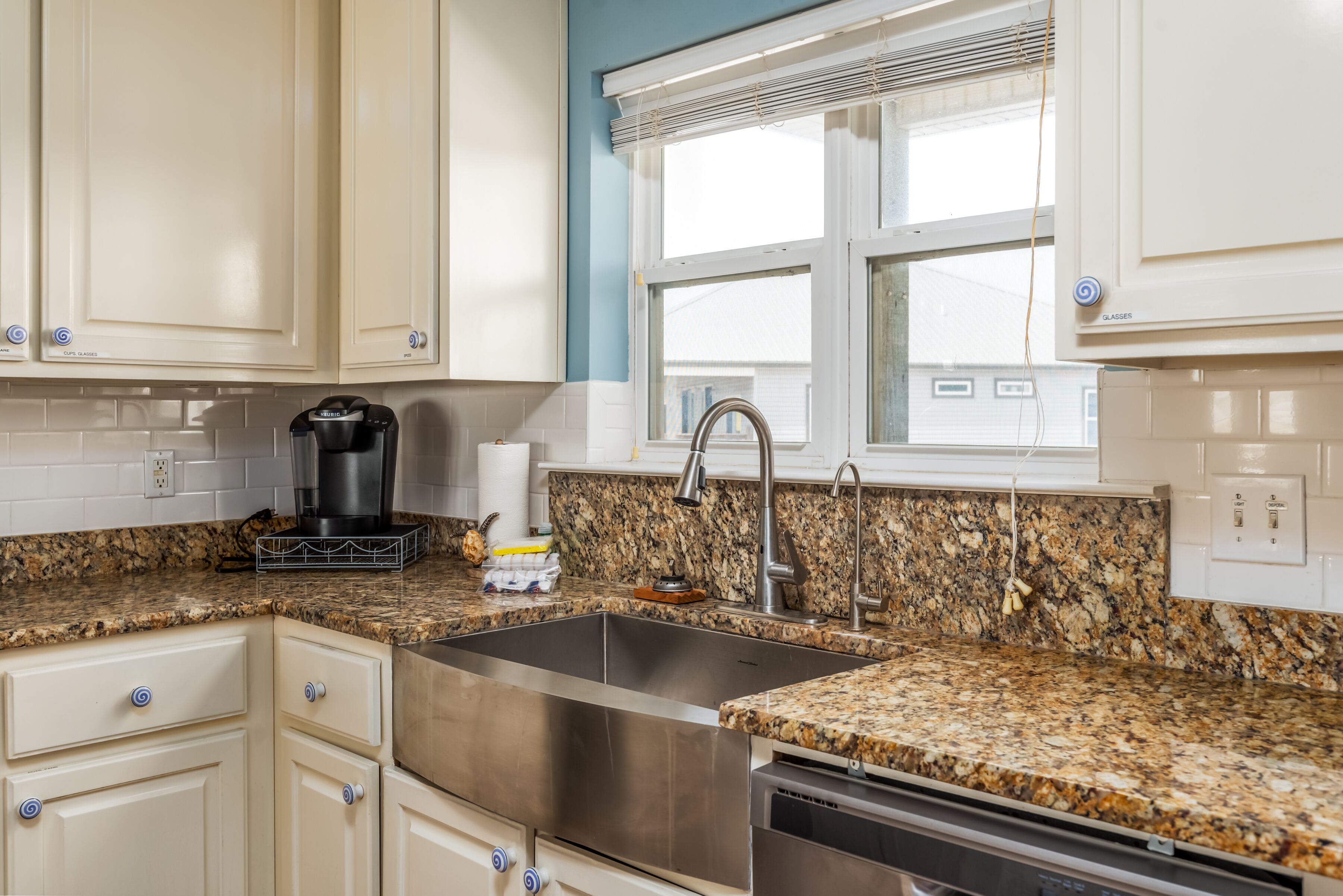 A kitchen with white cabinets, a granite countertop, stainless steel sink, and a coffee maker.