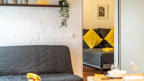 Un salon moderne avec un canapé gris, une petite table sur laquelle on a posé des fruits et un mur en briques blanches.