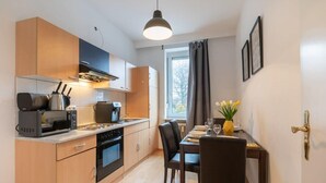Een compacte keuken met moderne apparaten, een eethoek met een tafel en stoelen, en een raam met gordijnen.