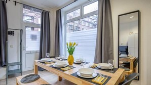 Comedor con mesa de madera preparada para cuatro personas, un florero con flores amarillas y vistas a edificios a través de amplios ventanales.