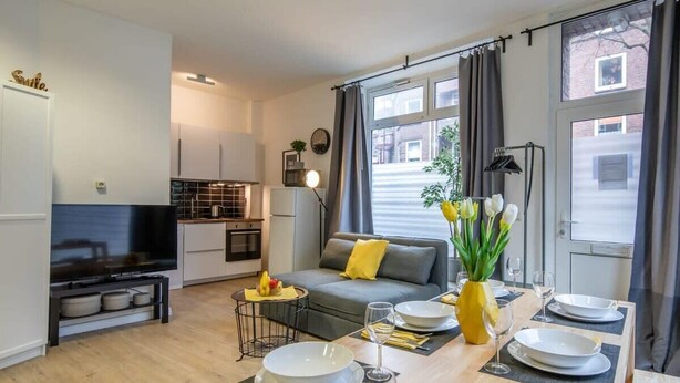 Una sala de estar moderna con un sofá, una mesa de comedor dispuesta para cuatro personas y una cocina al fondo.