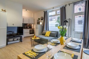 A modern living room with a sofa, dining table set for four, and a kitchen in the background. - Studio Family Loft  Self CheckIn  Street Parking (Hamburg)