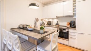 Une cuisine moderne avec des meubles blancs, un îlot central doté de sièges, une machine à café et un four encastré.