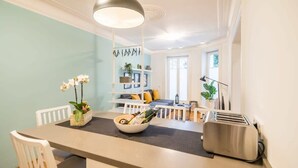 Une cuisine moderne avec un îlot central, des chaises blanches, un saladier de fruits et un grille-pain.