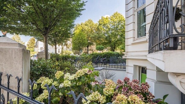 Une cour intérieure agrémentée d’une grille en fer forgé, d’une végétation luxuriante et d’un bâtiment doté d’un balcon.