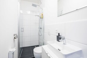 Une salle de bain moderne avec une douche à parois de verre, des toilettes blanches et un lavabo blanc doté d’un distributeur de savon noir.