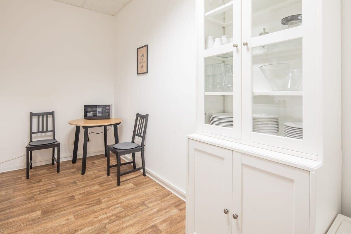 Un petit coin repas avec une table ronde et deux chaises, un buffet blanc aux portes vitrées et un four à micro-ondes fixé au mur.