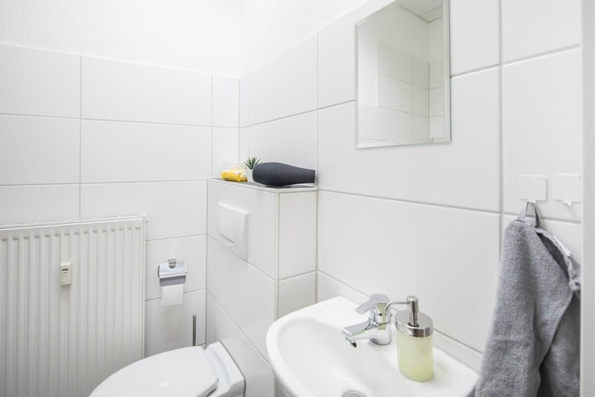A modern bathroom with a white sink, a mirror, a towel rack, and a toilet.