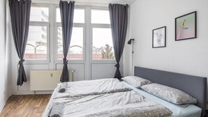 Une chambre à coucher avec un lit, des rideaux, un radiateur et deux tableaux encadrés accrochés au mur.