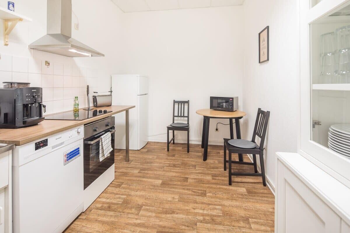 Eine kompakte Küche mit Geschirrspüler, Backofen, Mikrowelle und einer kleinen Essecke mit zwei Stühlen und einem Tisch.
