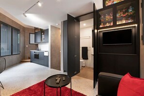 Un espace de vie moderne comprenant une cuisine, un coin repas et un téléviseur fixé à un mur de couleur sombre.